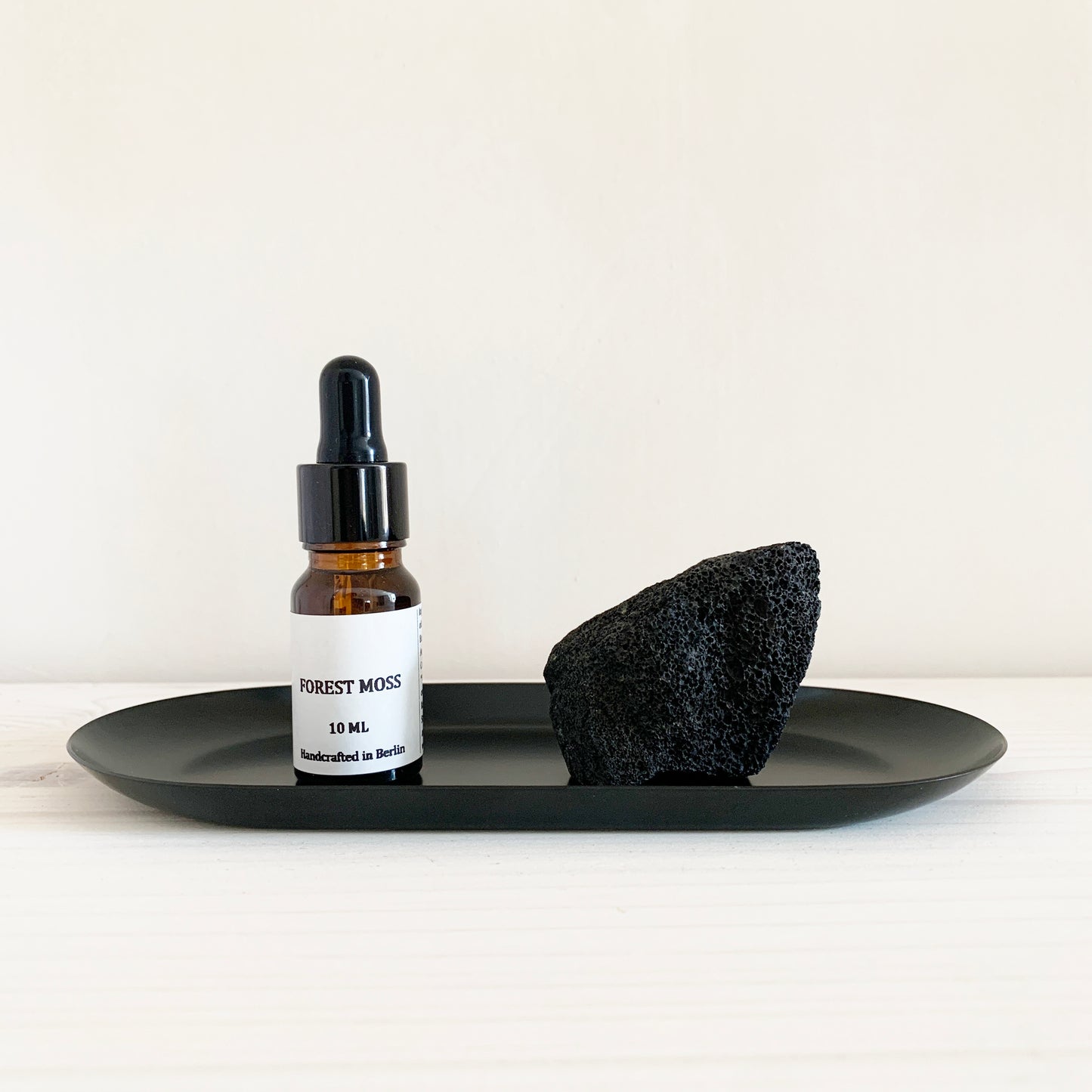 An essential oil diffuser set featuring a small bottle labeled 'FOREST MOSS' and a black lava stone on a larger black tray, all placed on a white surface.