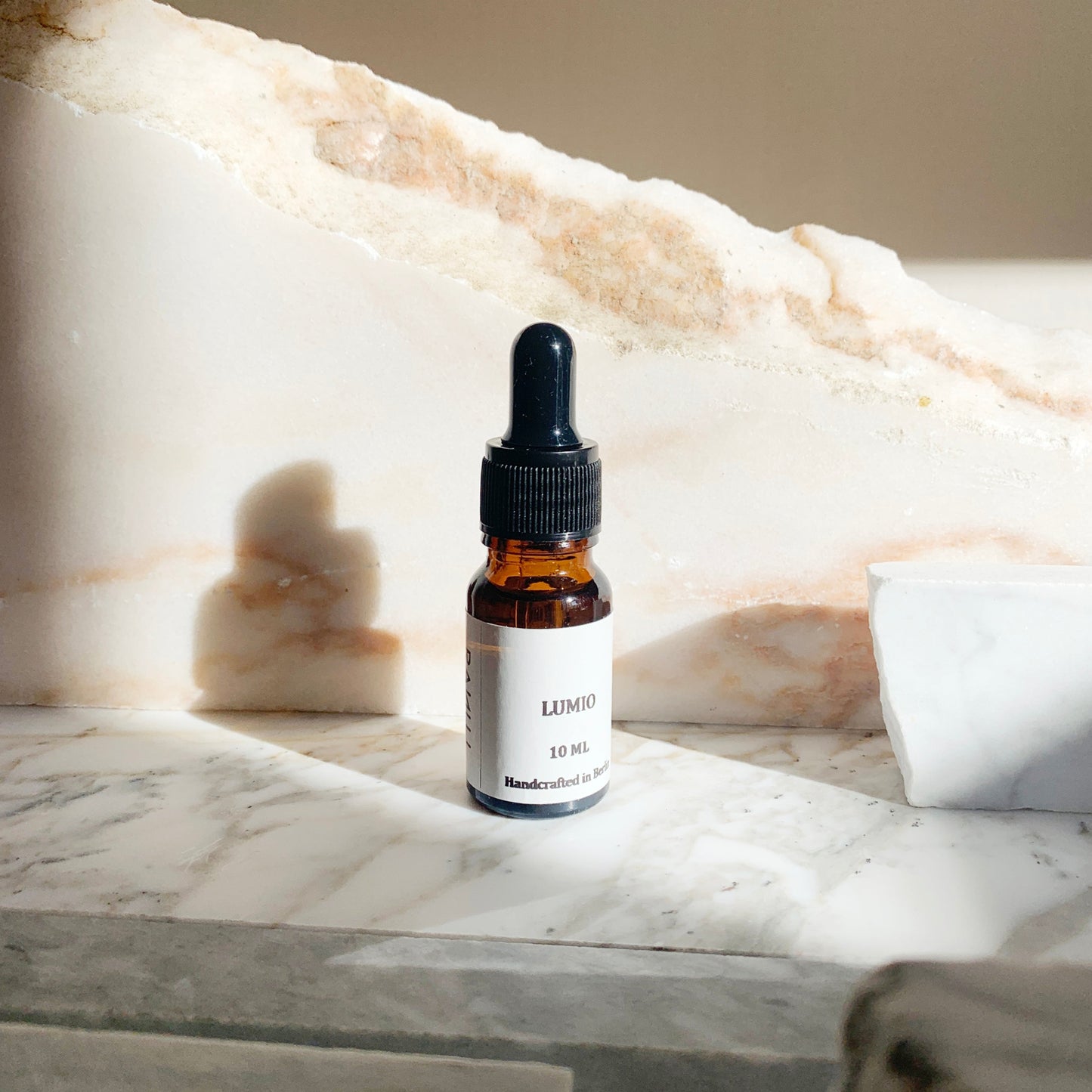 A 10ml essential oil dropper bottle with a white label LUMIO, placed on a marble surface.