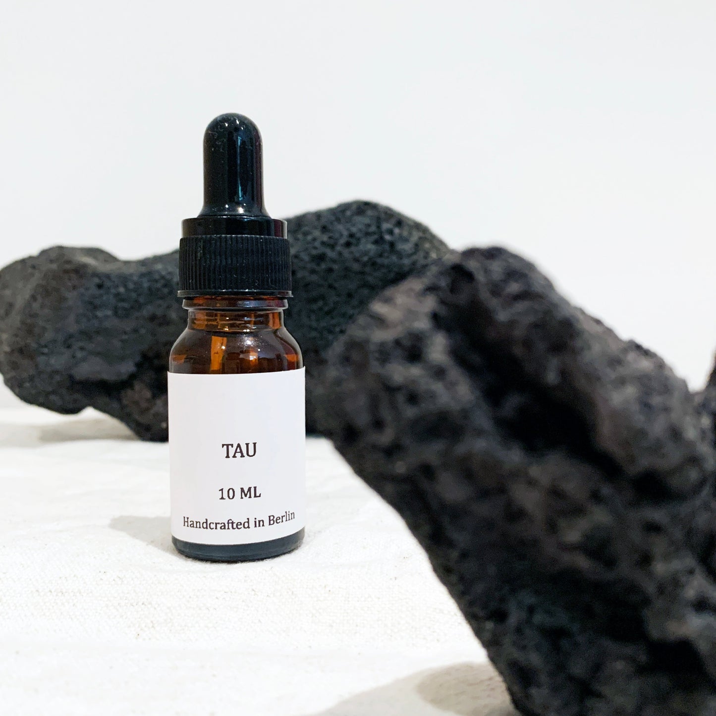 Essential oil blend bottle labeled 'TAU' with a dropper on a white background