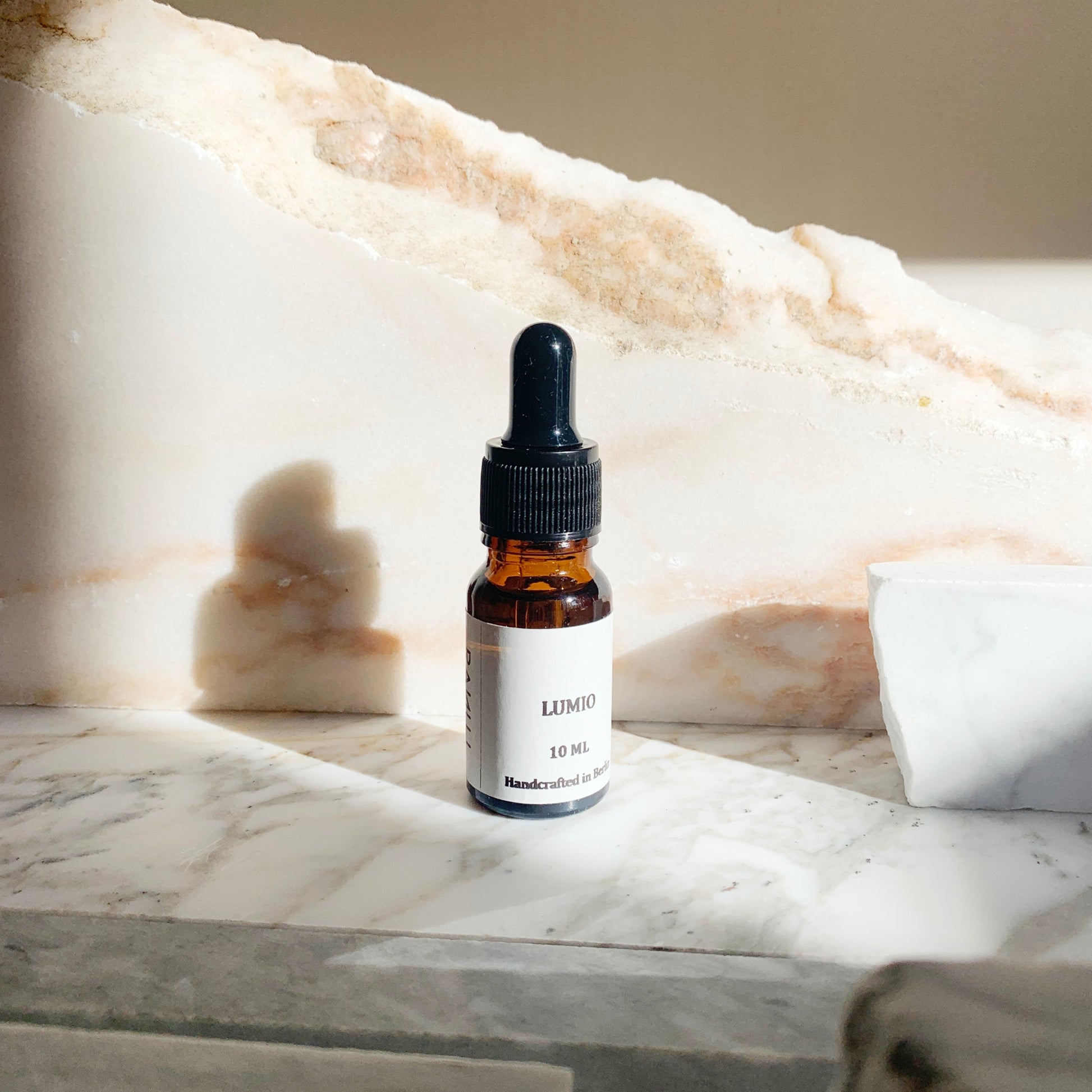 A 10ml essential oil dropper bottle with a white label LUMIO, placed on a marble surface.