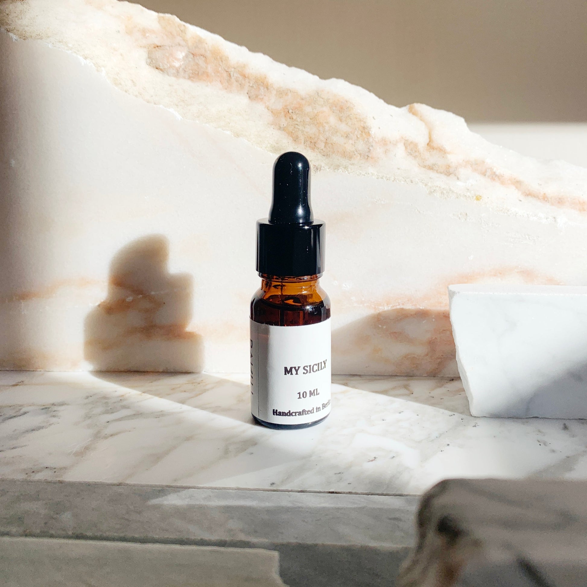 A 10ml bottle of MY SICILY essential oil blend placed on a marble surface, with a white and beige background suggesting a calm and luxurious setting.