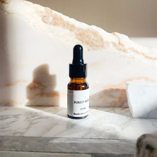 A 10ml bottle of FOREST MOSS essential oil blend placed on a marble surface, with a white and beige color scheme in the background.