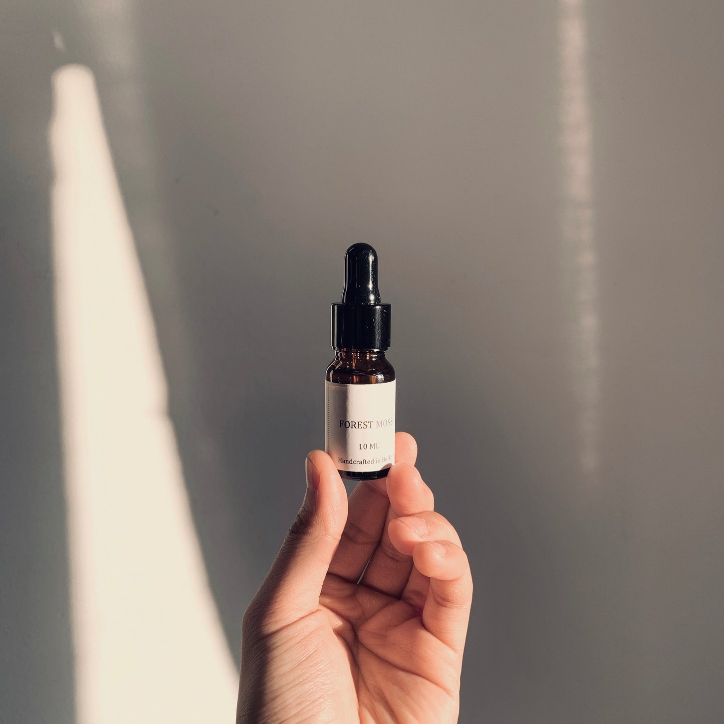 Hand holding a small black dropper bottle against a neutral background