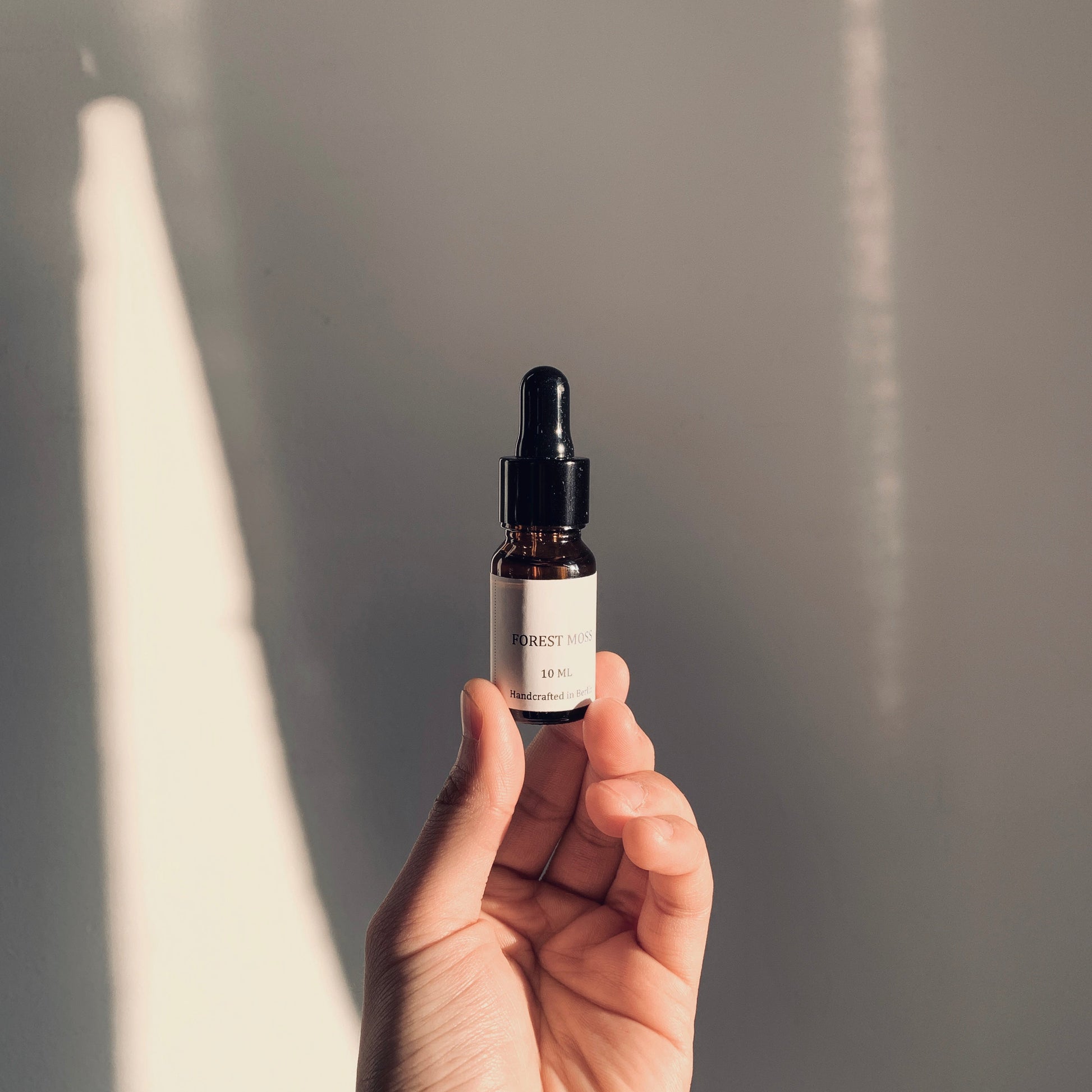 Hand holding a small black dropper bottle against a neutral background