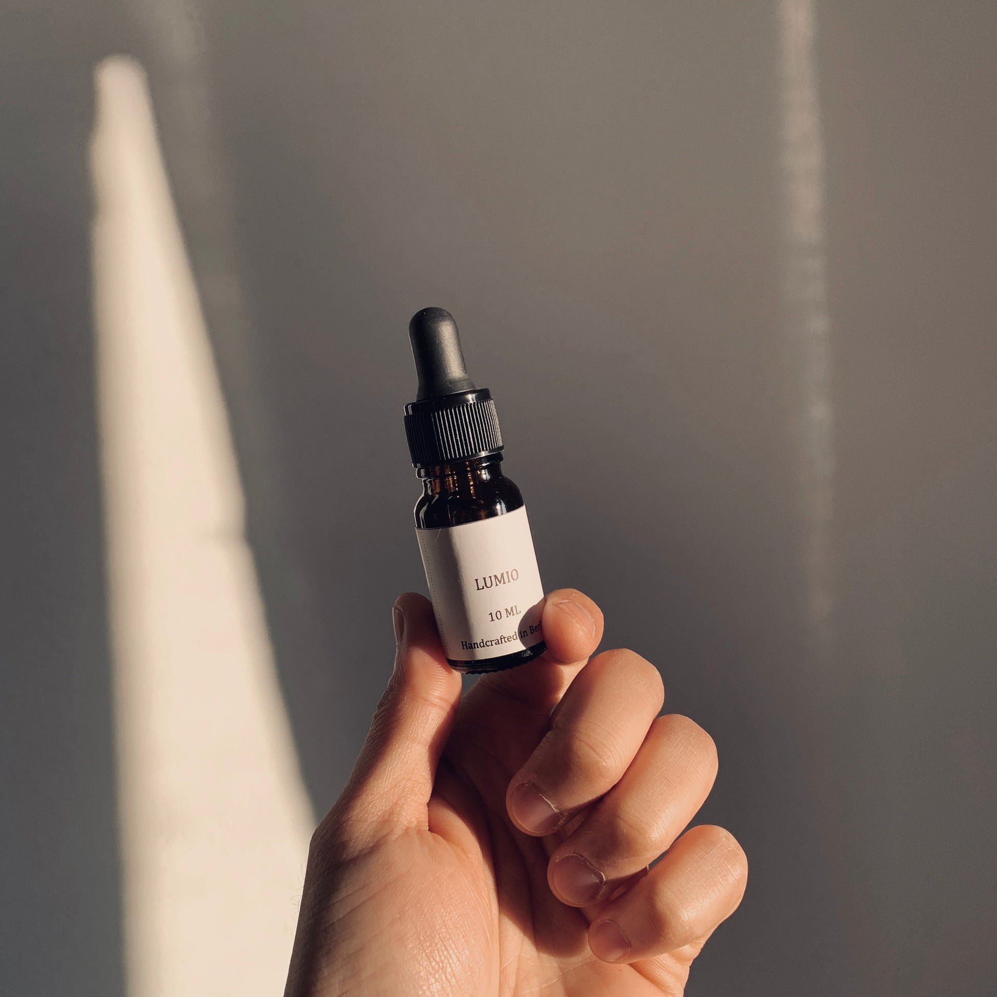 Hand holding a small brown bottle with a dropper against a neutral background
