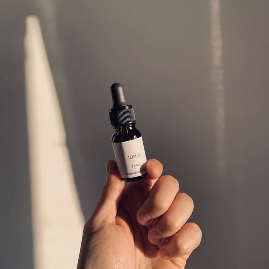 Hand holding a small brown bottle with a dropper against a neutral background