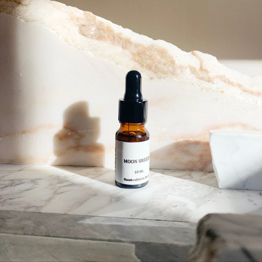 A 10ml bottle of MOON BREEZE essential oil blend placed on a marble surface, with a white and beige color scheme in the background.