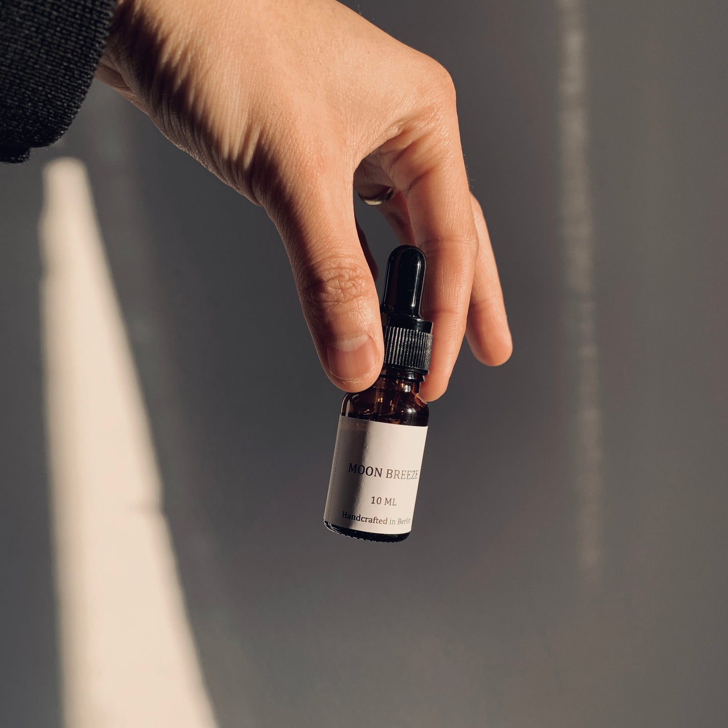 Hand holding a small black and white bottle against a neutral background