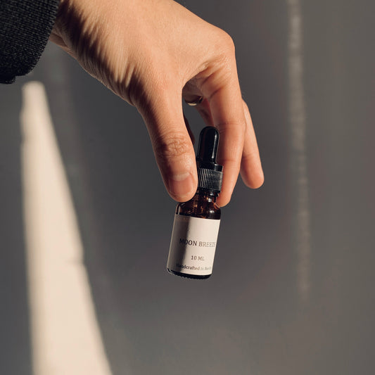Hand holding a small black and white bottle against a neutral background